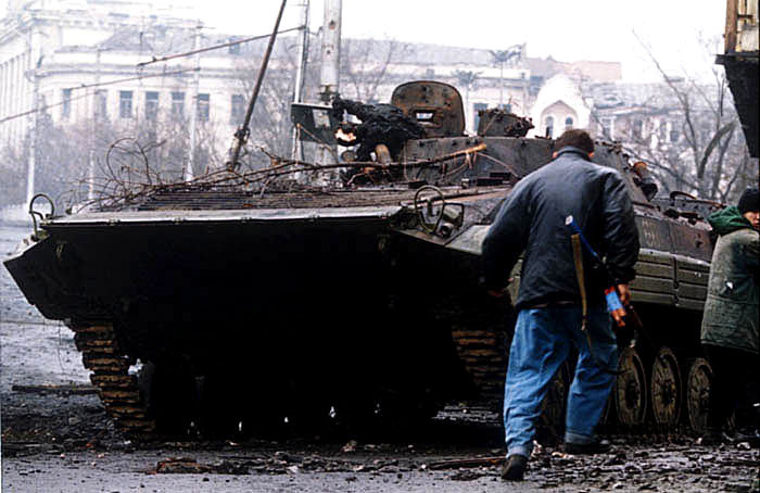 A Chechen fighter runs past a burnt-out Russian BMP-2 armoured vehicle during the battle for Grozny, First Chechen War